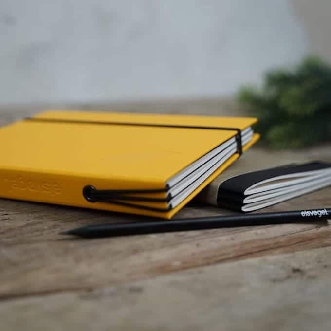 Yellow eisvøgel cover with three booklets fanned out of the spine, next to a branded pencil.