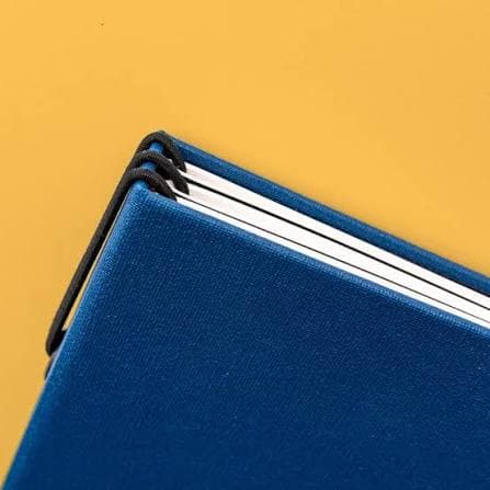Corner of a blue sealed-cotton cover showing the booklet block and elastic closure.